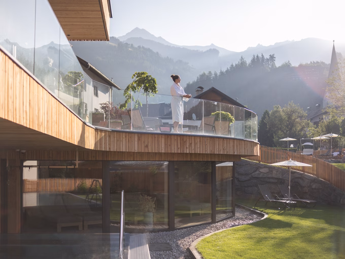 Eine Frau im Bademantel genießt den morgendlichen Ausblick vom geschwungenen Holzbalkon beim Naturhotel Outside in Matrei in Osttirol.