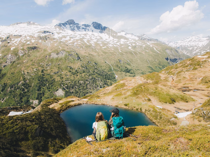 Zwei Wanderer sitzen auf Almboden und genießen Ausblick zu kleinem Bergsee - TVB Osttirol Elias Bachmann
