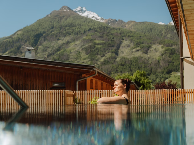 Eine Frau genießt die Sonne im Außenpool mit Blick auf die Osttiroler Bergwelt beim Naturhotel Outside in Matrei in Osttirol.