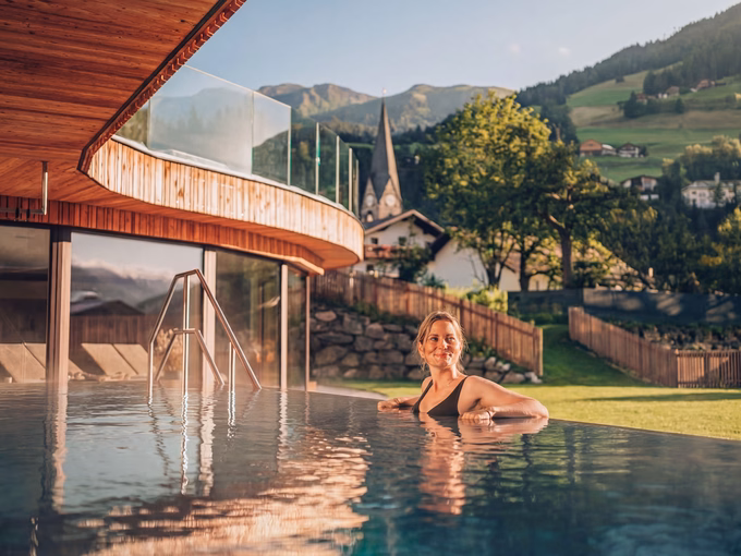 Eine Frau im beheizten Außenpool mit Blick auf den Kirchturm von Matrei beim Naturhotel Outside in Matrei in Osttirol.
