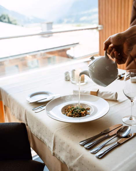 Servieren einer heißen Fritattensuppe aus einer weißen Kanne am Restauranttisch im Naturhotel Outside in Matrei in Osttirol