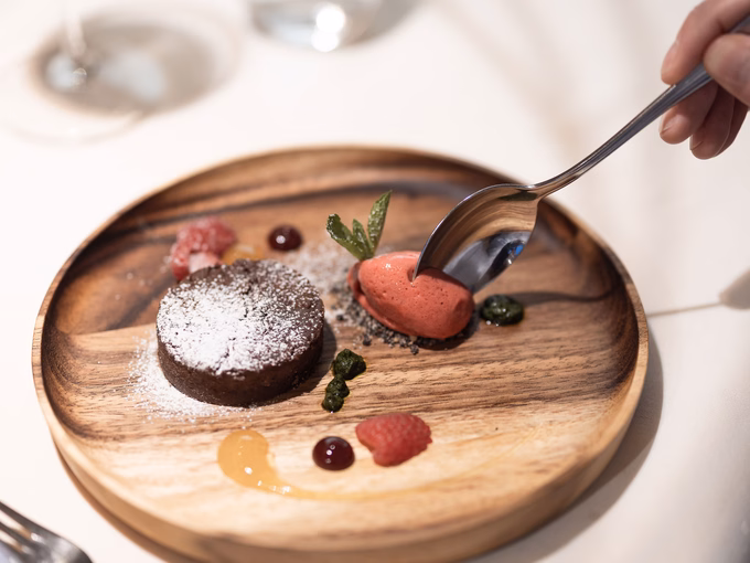 Ein Löffel nimmt eine Portion Erdbeersorbet von einem Dessert-Teller mit Schokoladentörtchen und Beeren im Naturhotel Outside in Matrei in Osttirol.