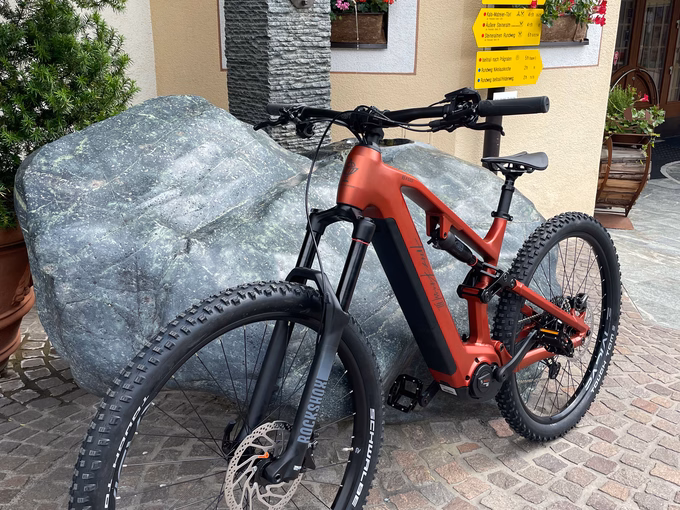 Ein rotes E-Mountainbike lehnt an einem Steinblock vor gelben Wegweisern beim Naturhotel Outside in Matrei in Osttirol