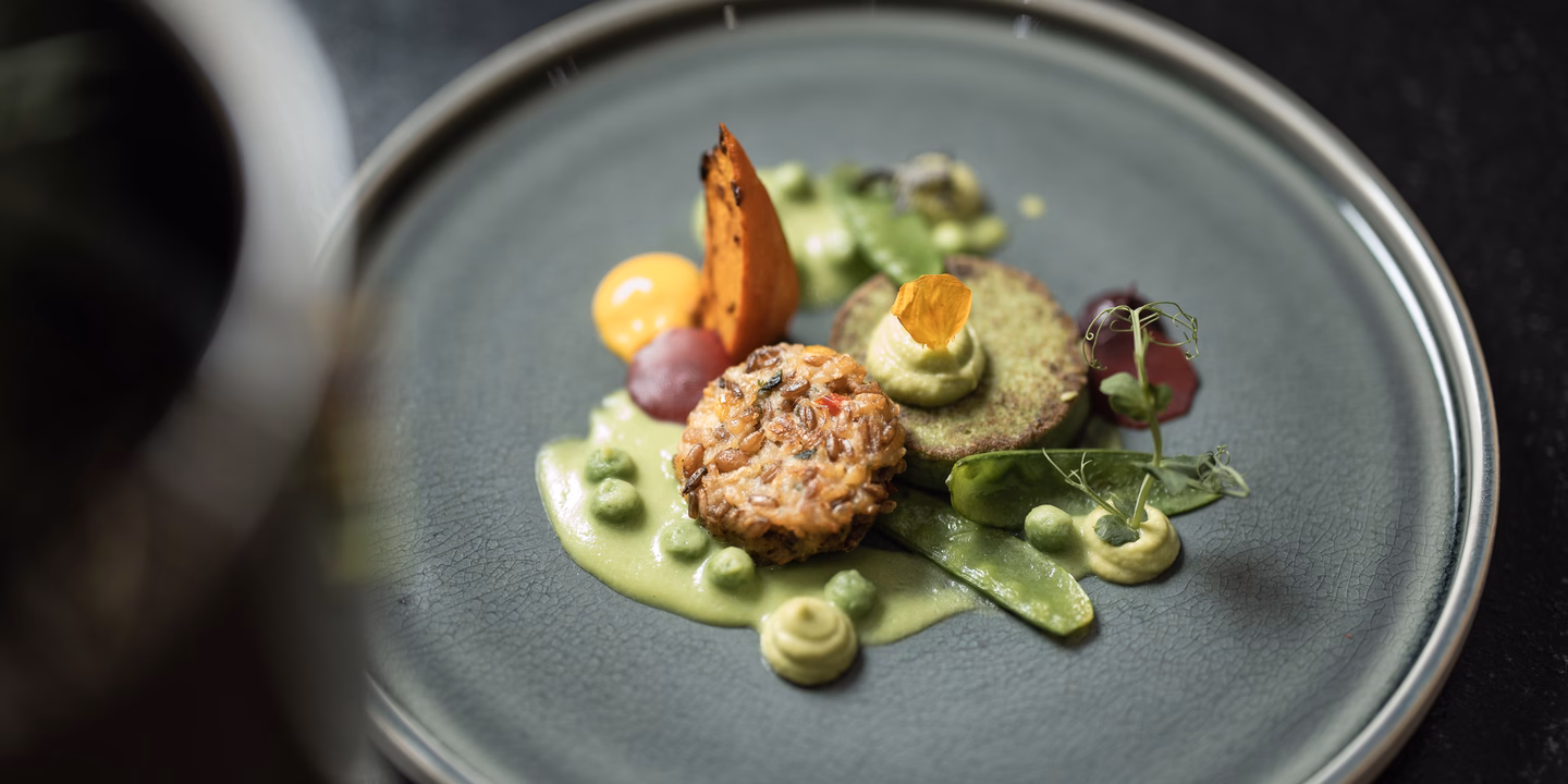 Nahaufnahme eines Tellers mit Buchweizenlaibchen, Kartoffelblini, Zuckerschoten und verschiedenen Erbsen-Texturen im Naturhotel Outside in Matrei in Osttirol.