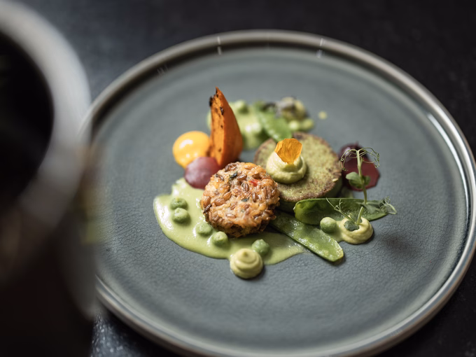 Nahaufnahme eines Tellers mit Buchweizenlaibchen, Kartoffelblini, Zuckerschoten und verschiedenen Erbsen-Texturen im Naturhotel Outside in Matrei in Osttirol.