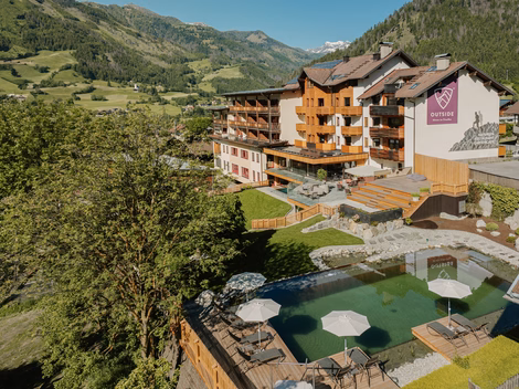 Vogelperspektive auf das Hotelgebäude, die Gartenanlage und den Naturbadeteich beim Naturhotel Outside in Matrei in Osttirol.