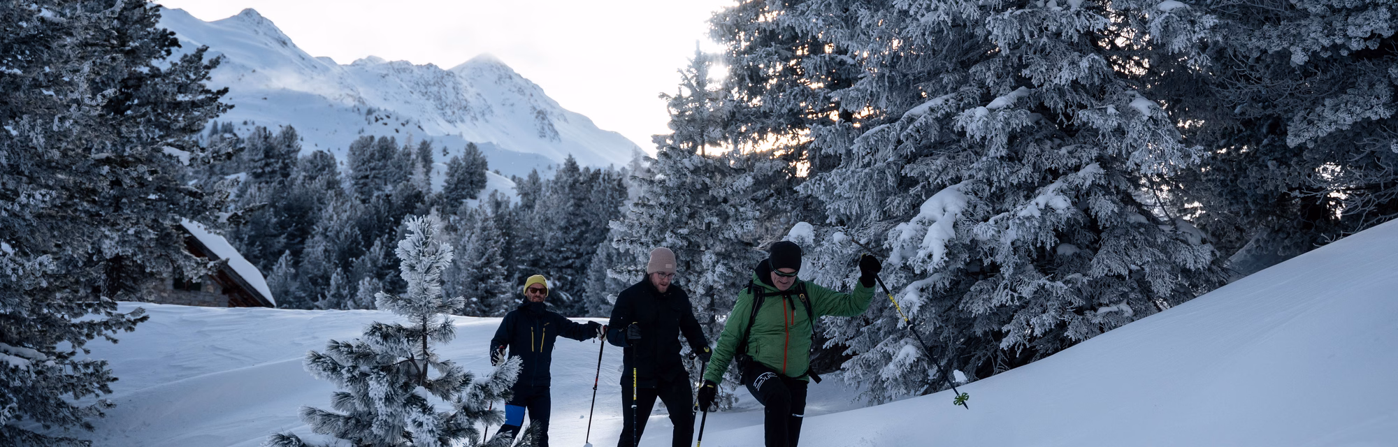 Drei Männer wandern mit Schneeschuhen und Stöcken einen steilen, tief verschneiten Hang am Waldrand hinauf, Naturhotel Outside in Matrei in Osttirol.