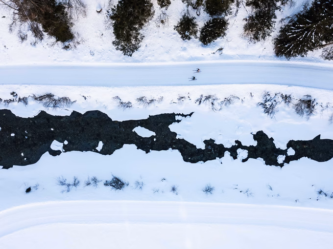 Drohnenaufnahme einer präparierten Langlaufloipe entlang eines schneebedeckten Gebirgsbachs in Osttirol.