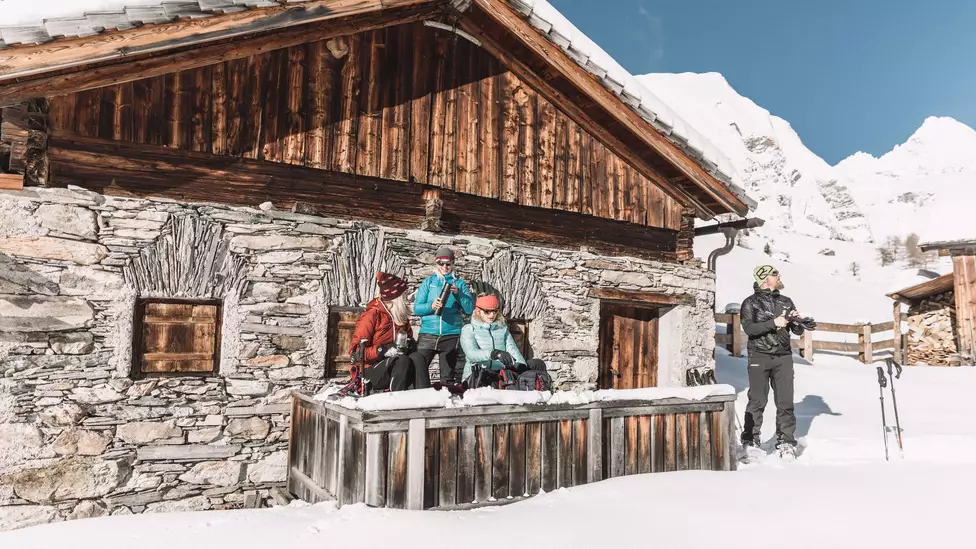 Schneeschuhwanderer machen Pause vor uriger Hütte in Kals