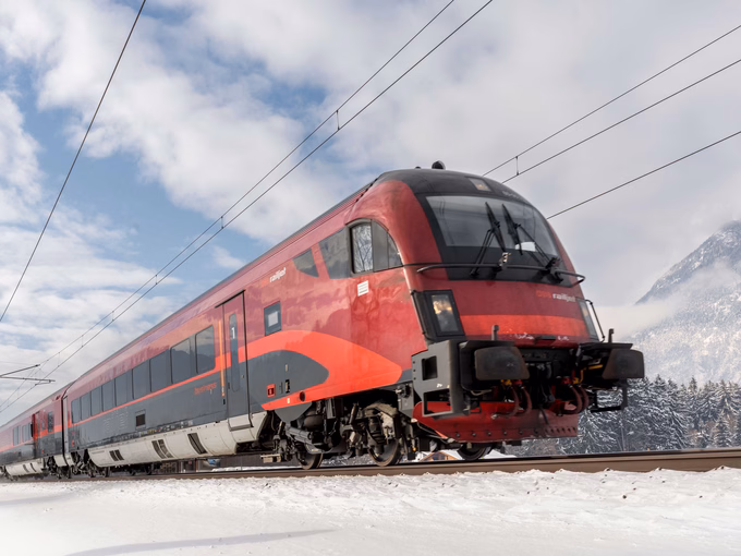 Roter ÖBB Railjet fährt durch eine verschneite Alpenlandschaft in Österreich.