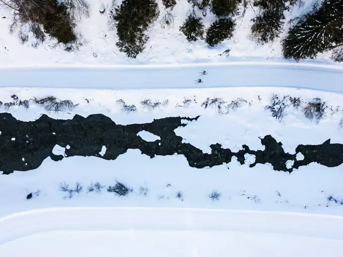 Blick aus Vogelperspektive auf zwei Langläufer auf Loipe am zugefrorenen Gebirgsbach