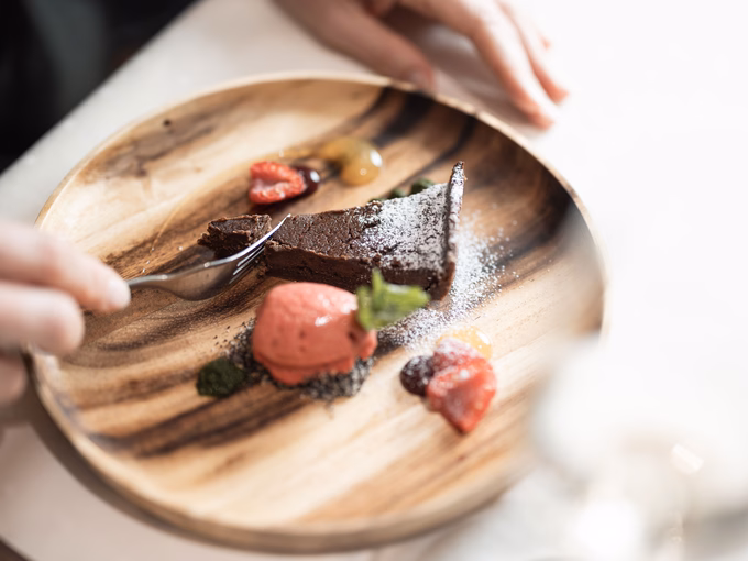 Nahaufnahme einer Schokoladentarte, die mit einer Gabel geteilt wird, serviert mit Erdbeersorbet und Früchten im Naturhotel Outside in Matrei in Osttirol.