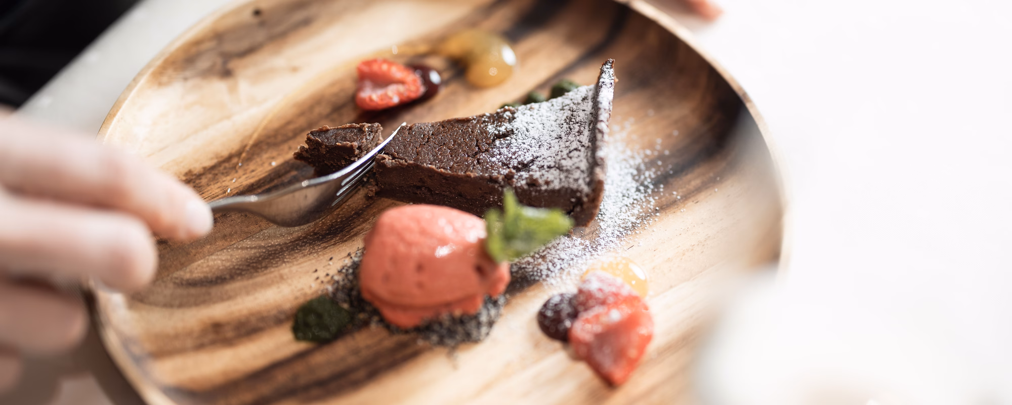 Nahaufnahme einer Schokoladentarte, die mit einer Gabel geteilt wird, serviert mit Erdbeersorbet und Früchten im Naturhotel Outside in Matrei in Osttirol.