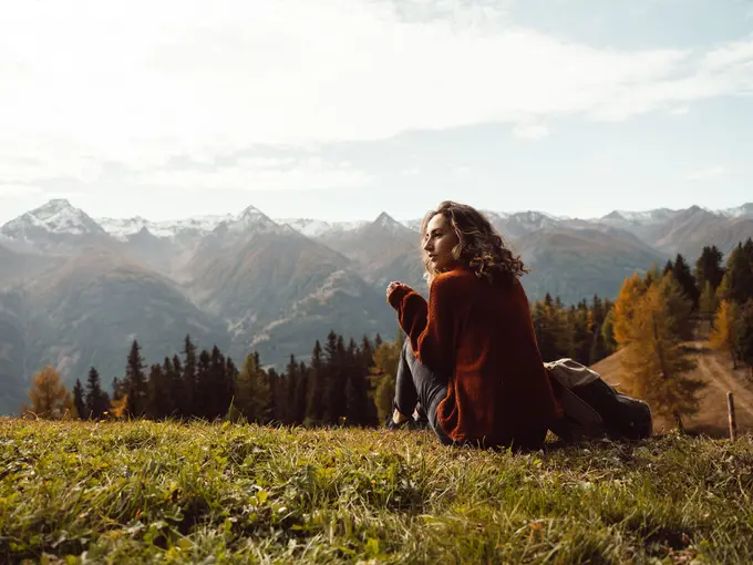 Frau sitzt auf Almwiese in der herbstlichen Berglandschaft
