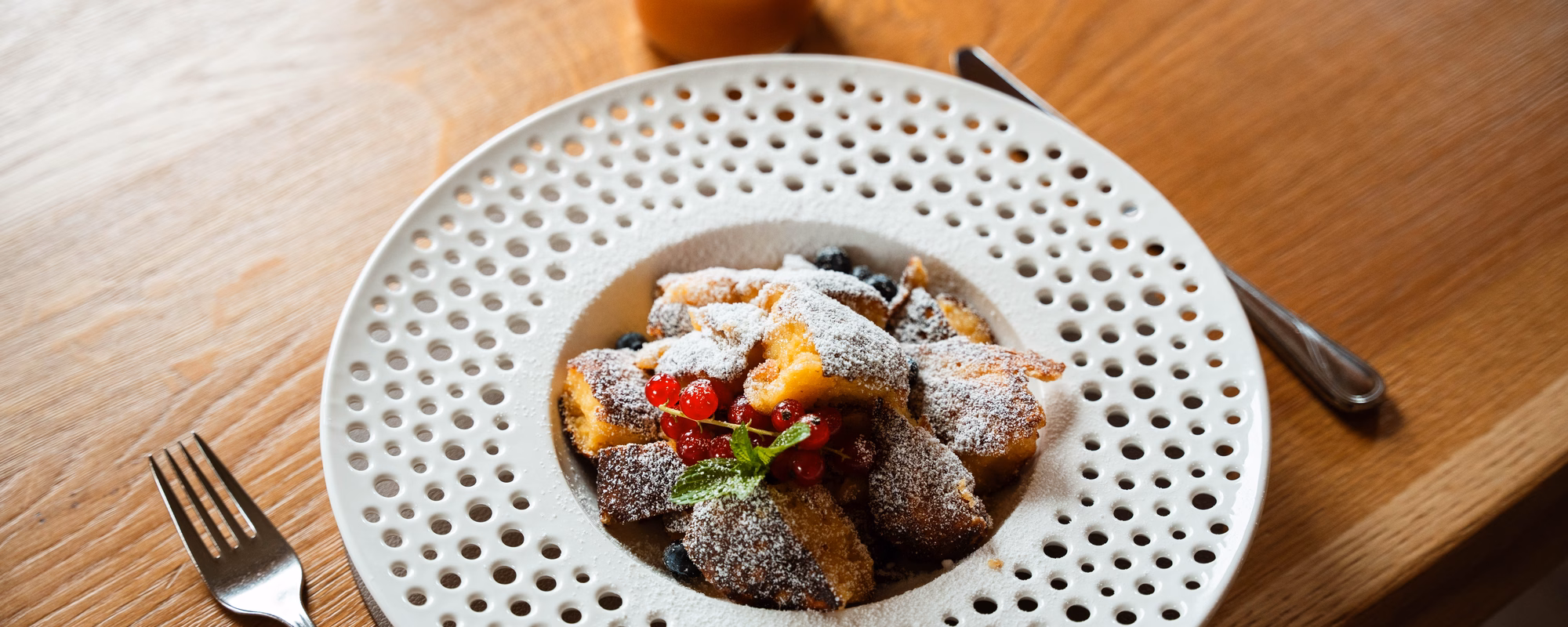 Klassischer Kaiserschmarrn mit Besteck und Apfelmus auf einem hellen Holztisch im Naturhotel Outside in Matrei in Osttirol