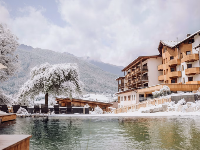 Blick über den hoteleigenen Naturbadeteich auf die verschneite Gartenanlage und das Hauptgebäude vom Naturhotel Outside in Matrei in Osttirol.