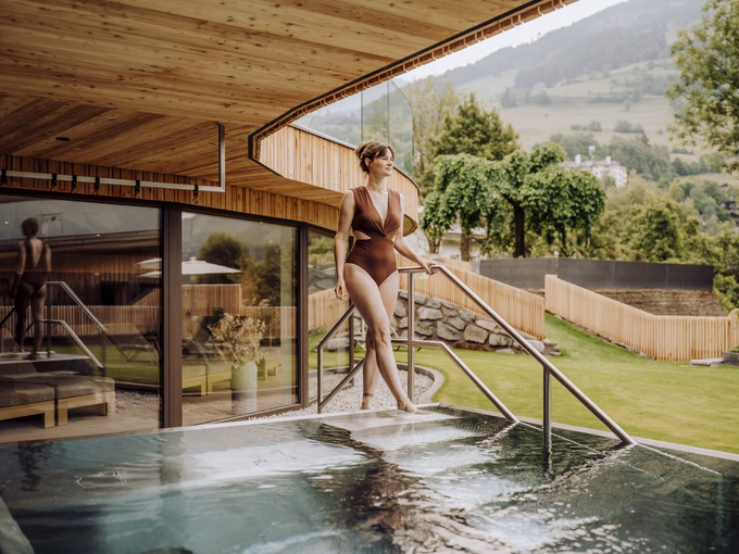 Blick über den Poolrand auf die Gartenmöbel und die umliegende Landschaft beim Naturhotel Outside in Matrei in Osttirol.