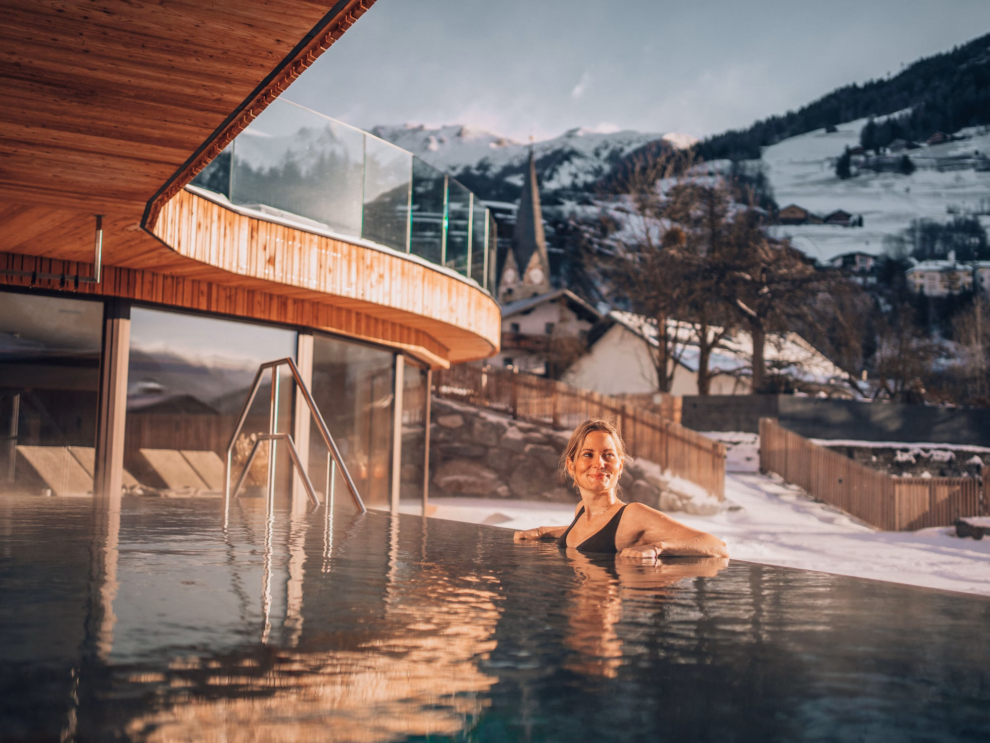 Lächelnde Frau im dampfenden Außenpool vor verschneiter Bergkulisse im Naturhotel Outside in Matrei in Osttirol