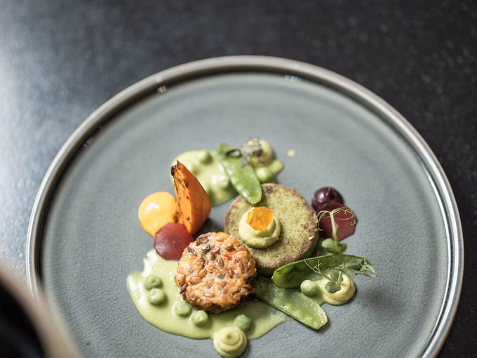 Draufsicht auf ein fertig angerichtetes vegetarisches Gericht mit Buchweizenlaibchen, Kartoffelblini und Erbsenpüree im Naturhotel Outside in Matrei in Osttirol.
