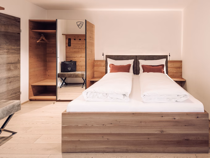 Doppelbett aus Naturholz mit roten Zierkissen und offenem Kleiderschrank im Bergzimmer im Naturhotel Outside in Matrei in Osttirol.