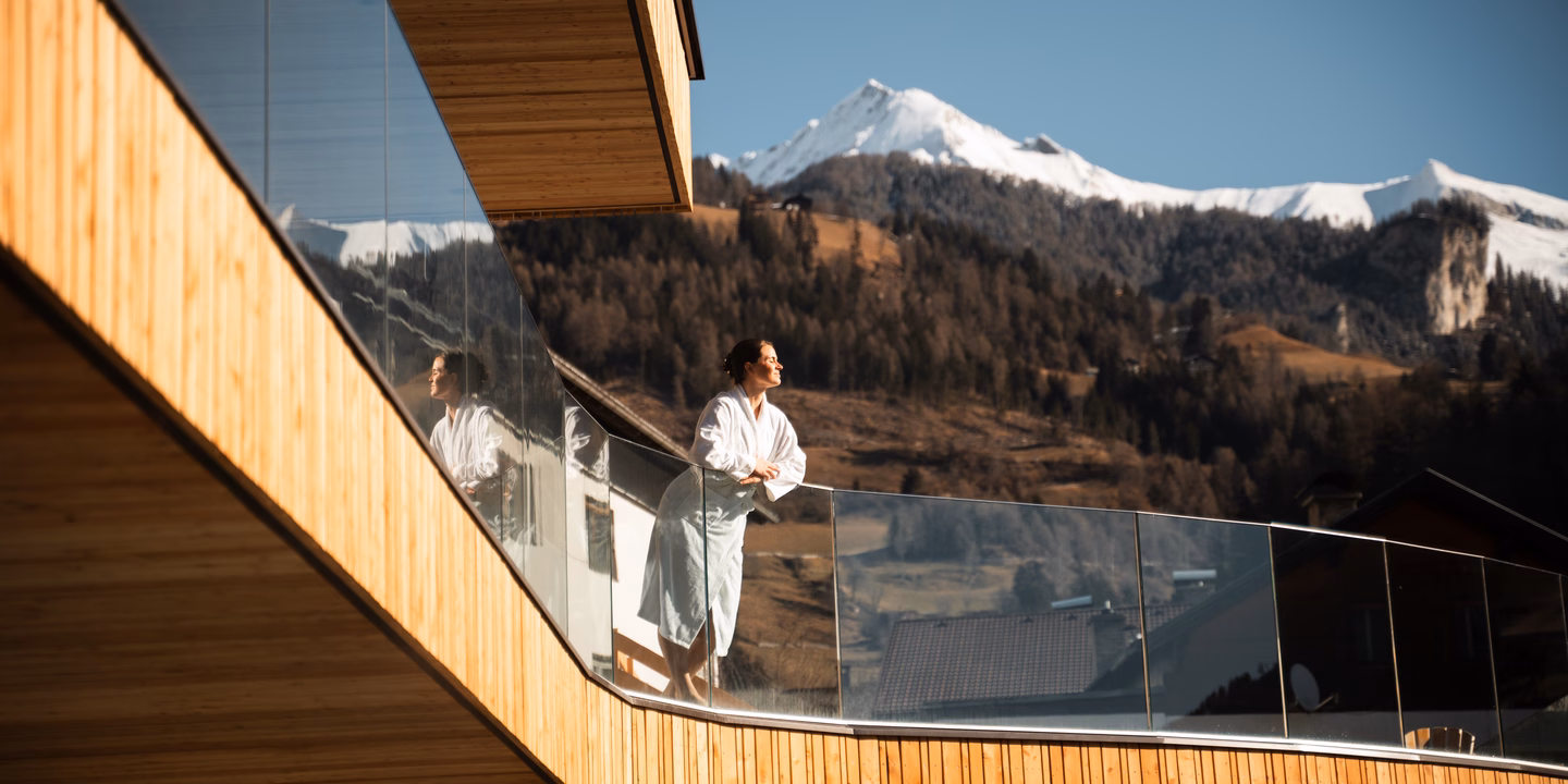 Eine Frau im Bademantel genießt die Sonne auf dem modernen Holzbalkon beim Naturhotel Outside in Matrei in Osttirol.