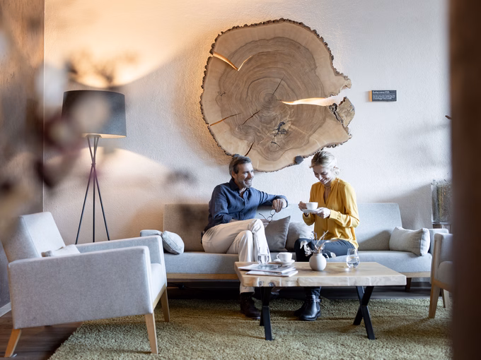 Ein Paar unterhält sich bei einer Tasse Kaffee in der Hotellobby mit markanter Wanddekoration aus Holz im Naturhotel Outside in Matrei in Osttirol
