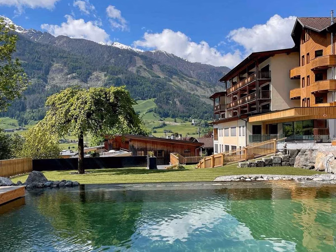 Ein chlorfreier Naturpool mit klarem Wasser vor der Kulisse der Osttiroler Berge beim Naturhotel Outside in Matrei in Osttirol.