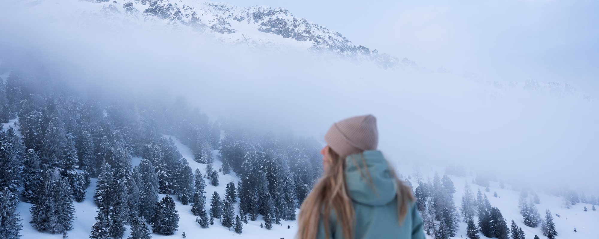 Blick über eine weite Winterlandschaft mit Tannen und einer kleinen Hütte unter einer dichten Wolkendecke, Naturhotel Outside in Matrei in Osttirol.