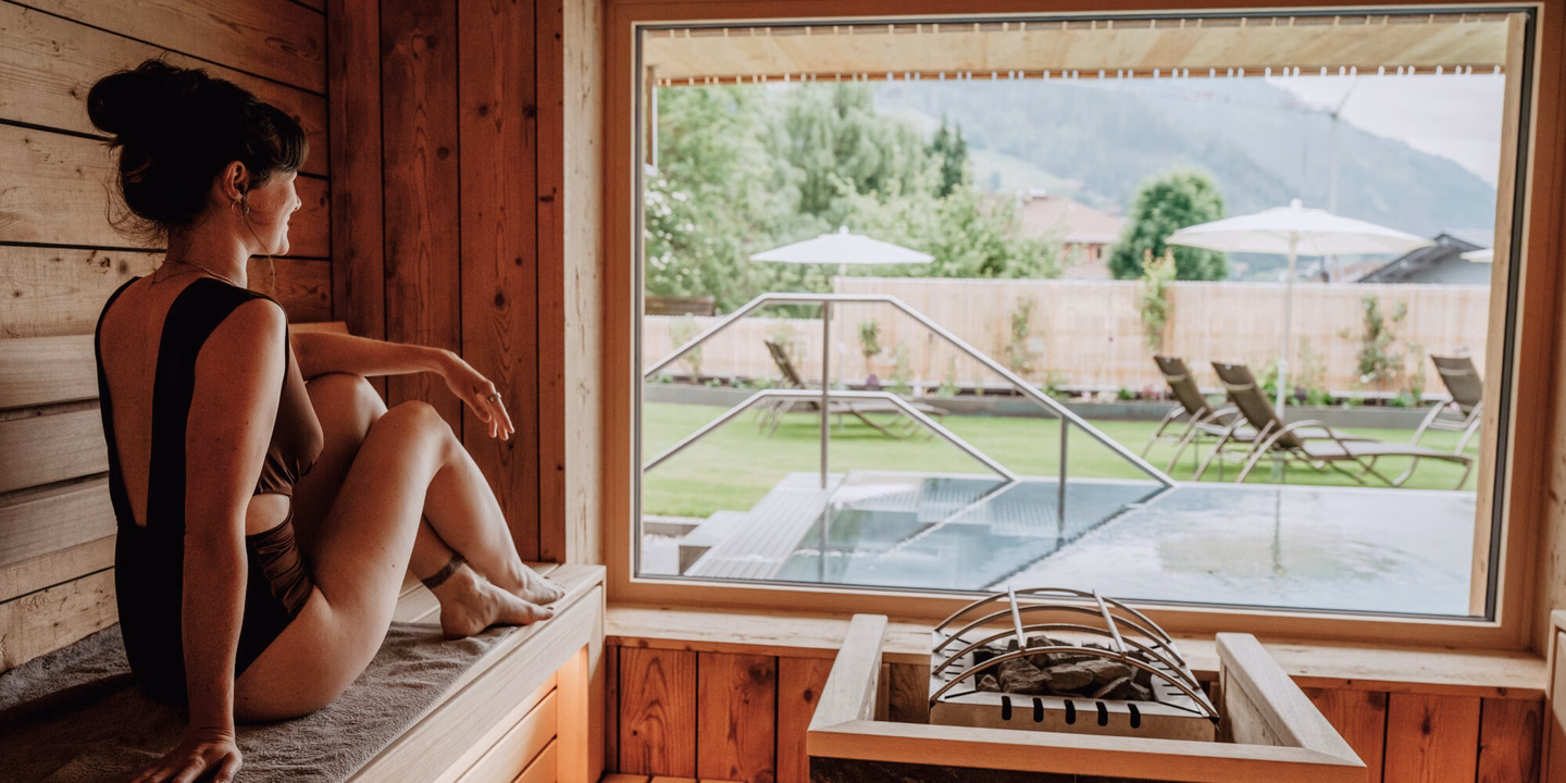 Sitzbereich in der Bio-Sauna mit Panoramafenster und Blick auf die Außenanlage im Naturhotel Outside in Matrei in Osttirol.