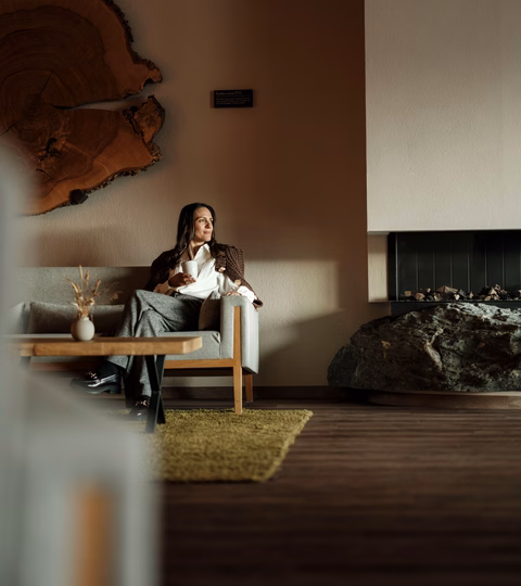 Frau mit Tasse auf dem Sofa neben dem Kamin in der Lobby im Naturhotel Outside in Matrei in Osttirol