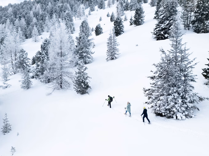Weitläufige Ansicht eines verschneiten Berghangs mit drei kleinen Figuren beim Schneeschuhwandern, Naturhotel Outside in Matrei in Osttirol.