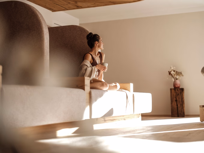 Frau mit Tasse auf einem modernen Daybed im Ruheraum im Naturhotel Outside in Matrei in Osttirol