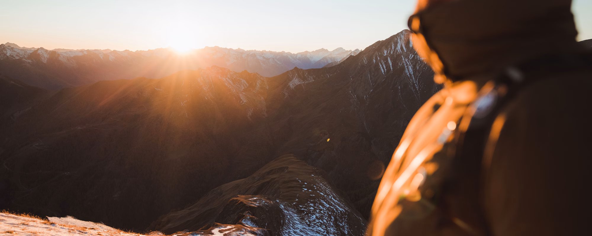 Mann steht am Berggipfel und genießt den Sonnenuntergang