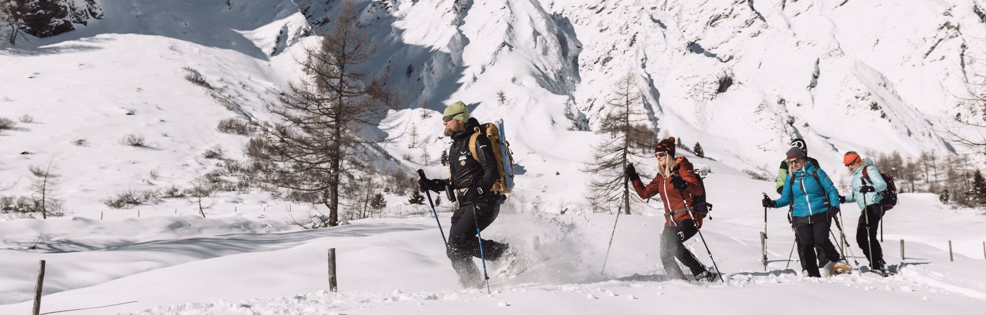 Ranger und Wandergruppe stapfen durch aufwirbelnden Pulverschnee vor verschneiter Bergkulisse in Kals am Großglockner.